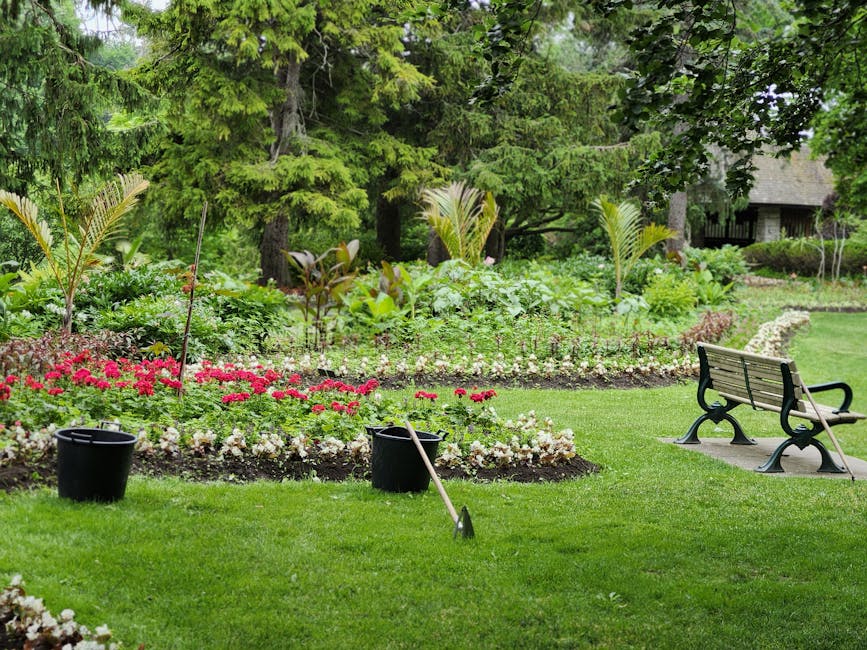 A well-maintained front garden featuring lush green grass with several flowerbeds bordered by dark, rich soil. The flowerbeds are filled with vibrant pink and white flowers, arranged in neat, curved l
